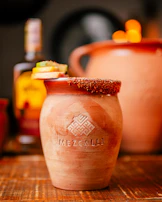 Close-up of mezcal poured into a traditional clay cup surrounded by dried agave plants.