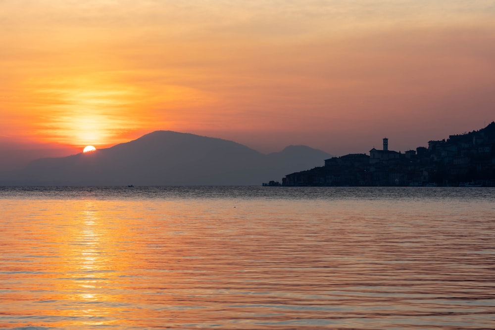 el sol se está poniendo sobre el agua con una ciudad a lo lejos