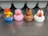 Four rubber duck toys are lined up on a metallic surface. Each duck is styled to resemble a different animal or character. The first duck wears a red cap and blue overalls, the second is painted pink to look like a pig, the third is brown with horse-like features, and the fourth is white with red details resembling a chicken.