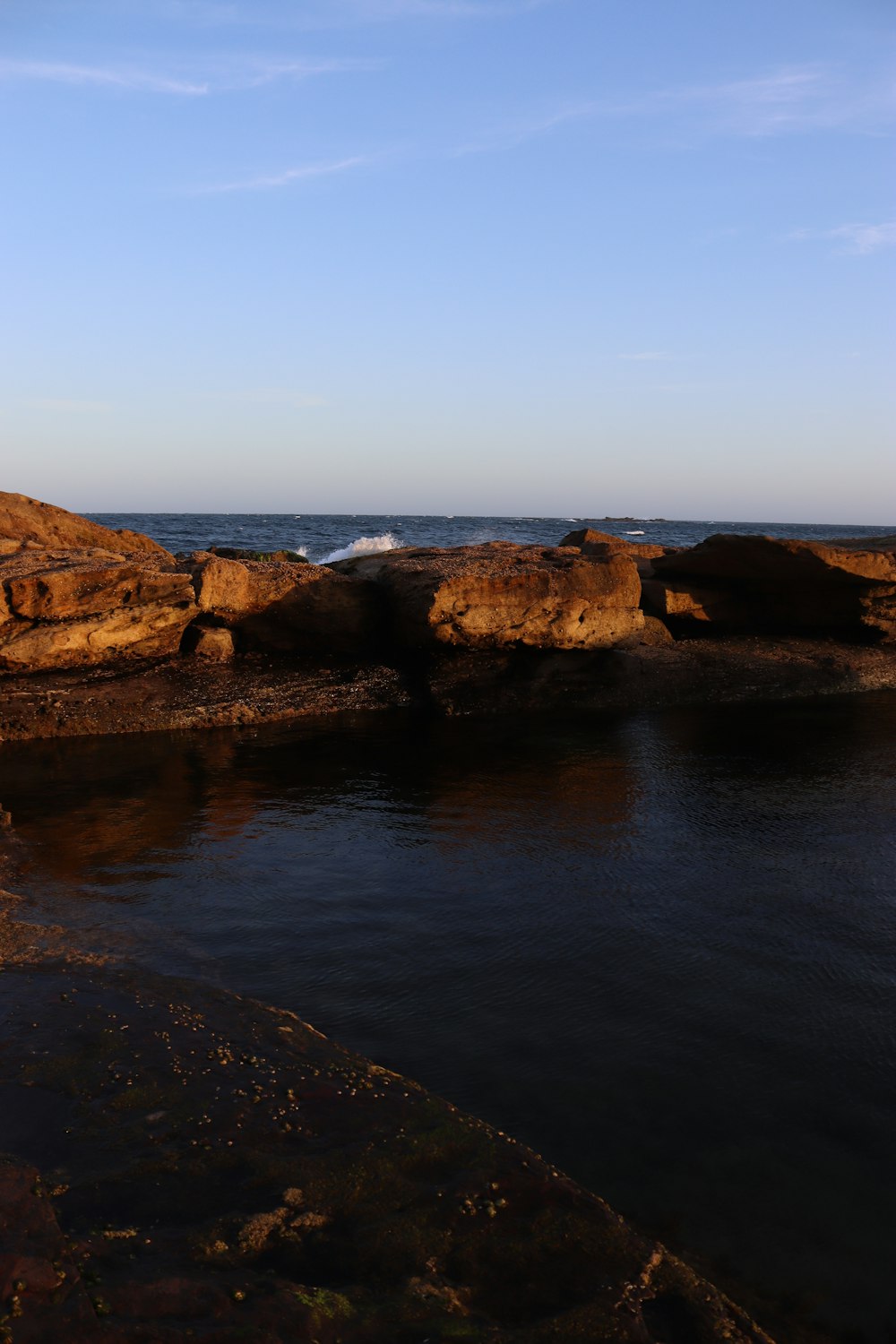 a body of water surrounded by rocks under a blue sky