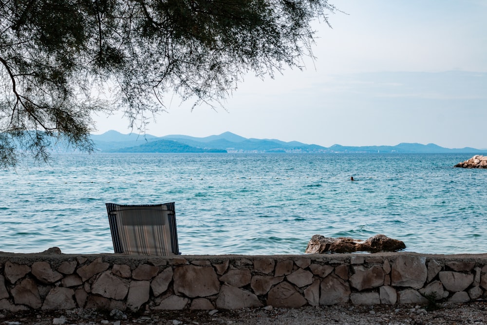 a wooden chair sitting on top of a stone wall next to a body of water