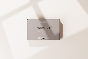 A minimalist travel kit box with the words 'travel kit' and 'mockup template' printed on it. The box is placed on a light surface with soft shadows cast across it.