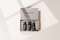 A beige travel kit box containing three small, black bottles neatly arranged inside. The kit includes items labeled as shampoo, conditioner, and a vitamin C serum. The minimalist packaging design is simple and elegant, with the words 'travel kit' and 'mockup template' clearly visible on the box. Soft shadows are cast on the surface, creating a subtle, natural lighting effect.