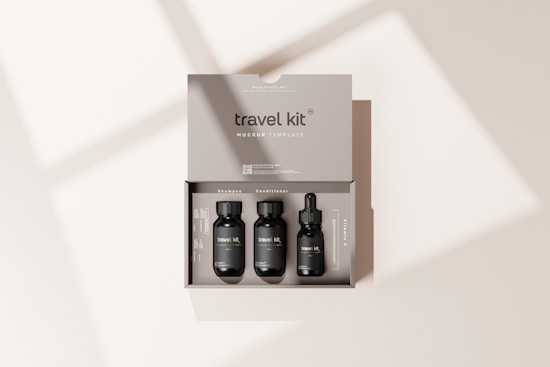 A beige travel kit box containing three small, black bottles neatly arranged inside. The kit includes items labeled as shampoo, conditioner, and a vitamin C serum. The minimalist packaging design is simple and elegant, with the words 'travel kit' and 'mockup template' clearly visible on the box. Soft shadows are cast on the surface, creating a subtle, natural lighting effect.