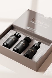 A close-up of an open box containing three small black bottles with labels that read 'travel kit'. The kit appears to be a mockup template or cosmetic set with a clean and minimalist design.