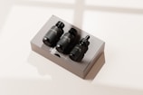 A set of three black bottles with droppers labeled as a travel kit, placed neatly on a rectangular, reflective, light-colored box. The scene is bathed in soft natural light, casting gentle shadows.