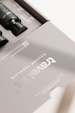 A sleek, modern packaging design featuring black bottles inside a matte gray box. The box is labeled 'Travel Kit' with clear, minimalistic typography. The design includes a QR code and some text detailing contents or instructions. The overall aesthetic is clean and sophisticated.