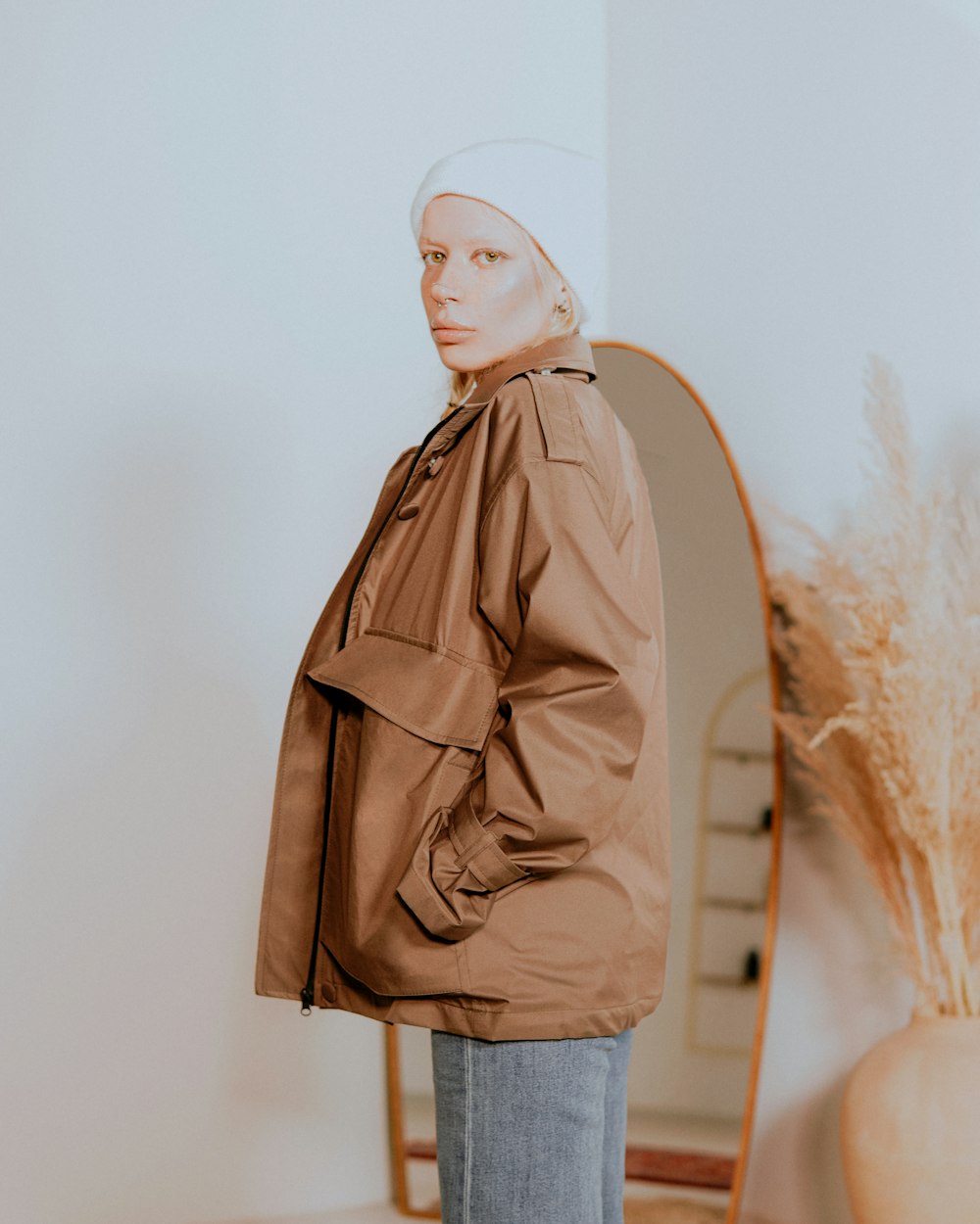 a woman standing in front of a mirror wearing a brown jacket