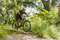 Close-up of a mountain biker navigating a rugged trail surrounded by lush forest.