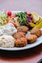 a plate of food that includes rice, meatballs, and salad