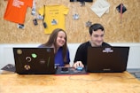 A boy and girl smiling as they work on homework together at a colorful table.