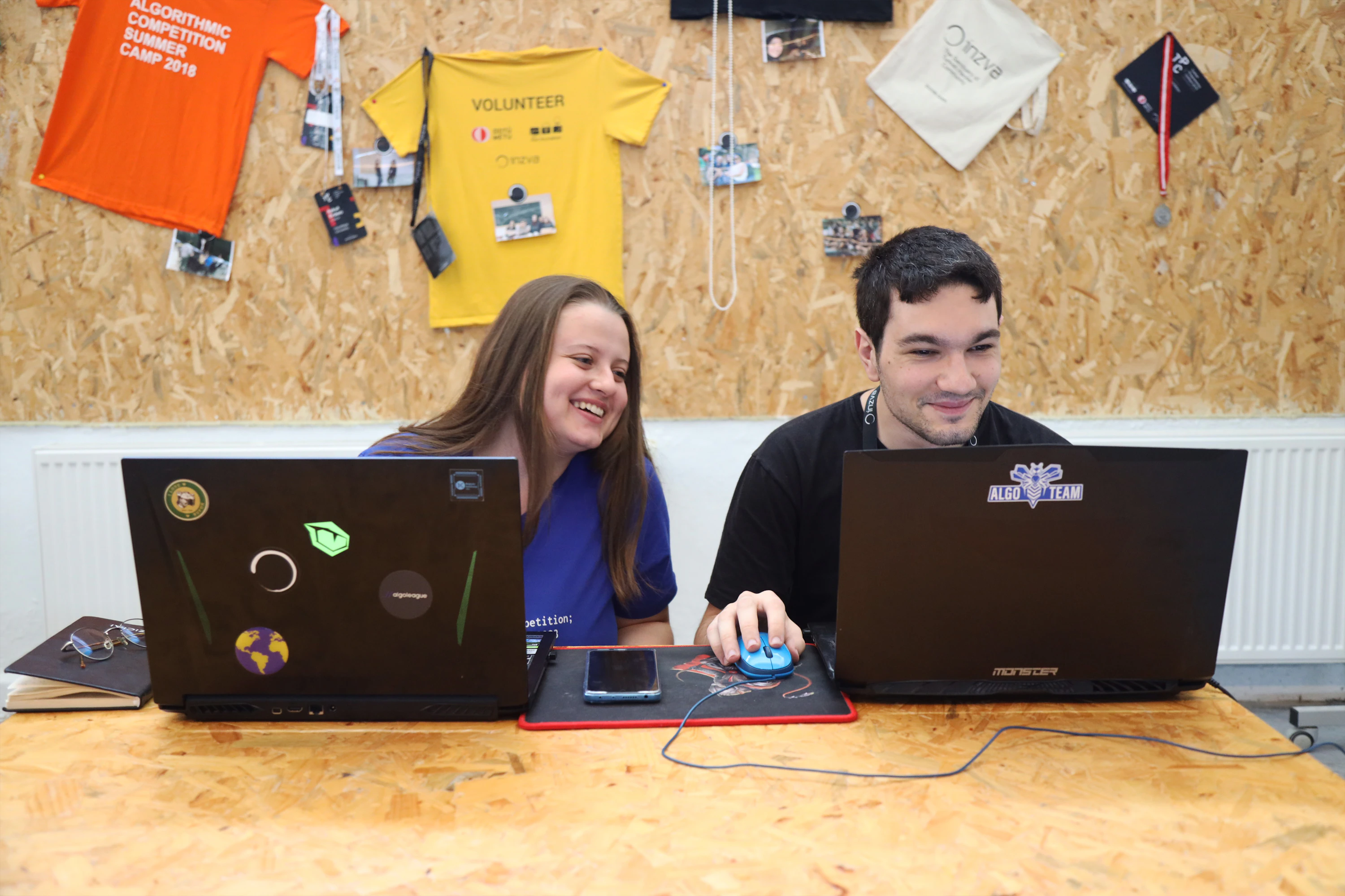 Two young volunteers smiling while working side by side on laptops
