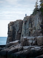 Adventurers climbing rocky coastal edges with the sea crashing below.