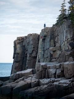 Adventurers climbing rocky coastal edges with the sea crashing below.