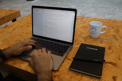 Close-up of a journalist typing an article on a laptop with a red and black branded mug nearby.