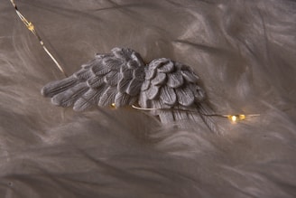 Close-up of a delicate angel wing embroidered on a soft, cream-colored fabric, glowing softly in natural light.