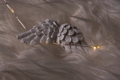 Close-up of a delicate angel wing embroidered on a soft, cream-colored fabric, glowing softly in natural light.