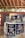 Several cans of flavored coffee, including charcoal and sea salt varieties, are arranged on a wooden table. The packaging features vibrant and colorful designs with cartoon characters. A box in the background displays more coffee cans, and some blurred text appears on a wall.