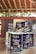 Several cans of flavored coffee, including charcoal and sea salt varieties, are arranged on a wooden table. The packaging features vibrant and colorful designs with cartoon characters. A box in the background displays more coffee cans, and some blurred text appears on a wall.