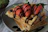 A close-up photo of a golden waffle topped with fresh strawberries, chocolate drizzle, and a scoop of vanilla ice cream on a rustic wooden table.