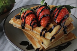 Close-up of a golden Belgian waffle topped with fresh strawberries and a drizzle of chocolate sauce
