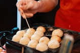 a person holding a stick over a tray of food