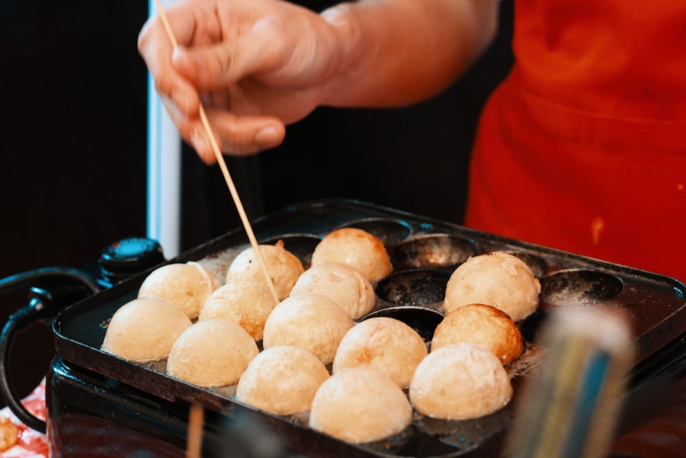 a person holding a stick over a tray of food