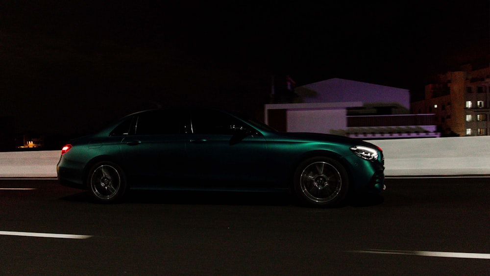 a green car driving down a street at night