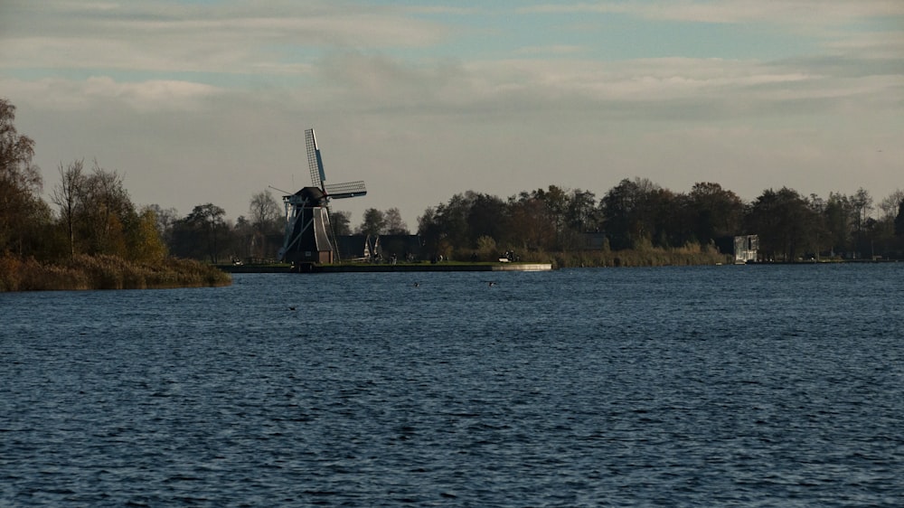 a windmill sitting on top of a lake next to a forest