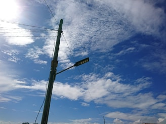 A professional electrician inspecting a street light pole against a clear sky.