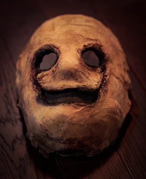 A rough papier-mâché mask drying on a rustic wooden table.