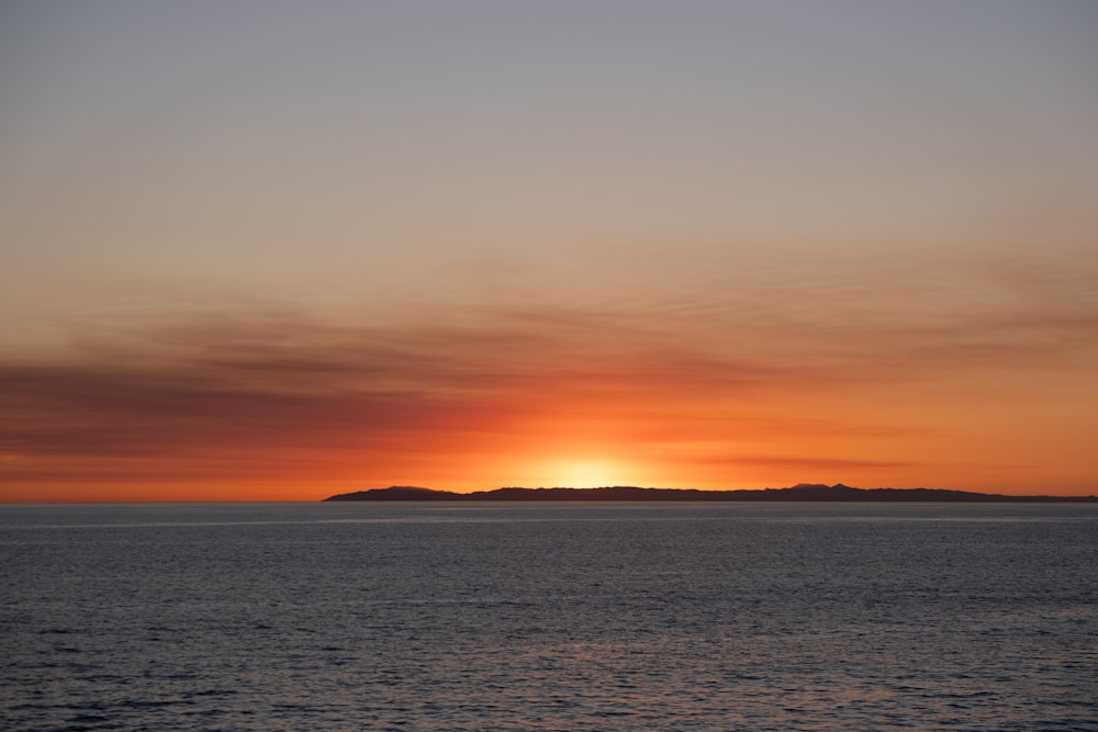 the sun is setting over the ocean with a small island in the distance