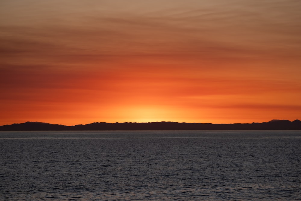 the sun is setting over the ocean with mountains in the distance