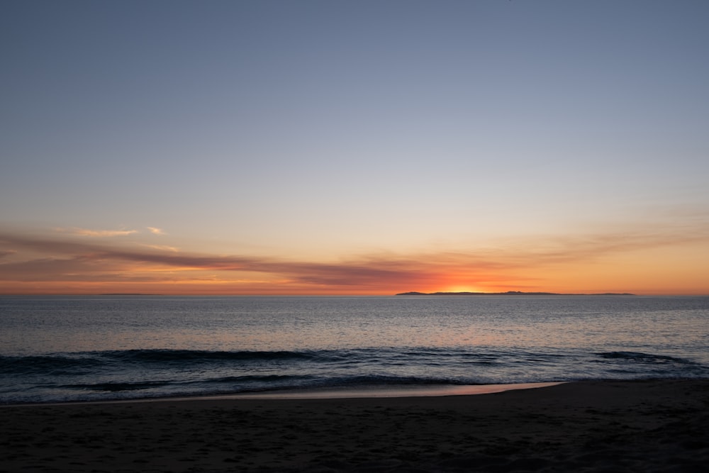 the sun is setting over the ocean on the beach