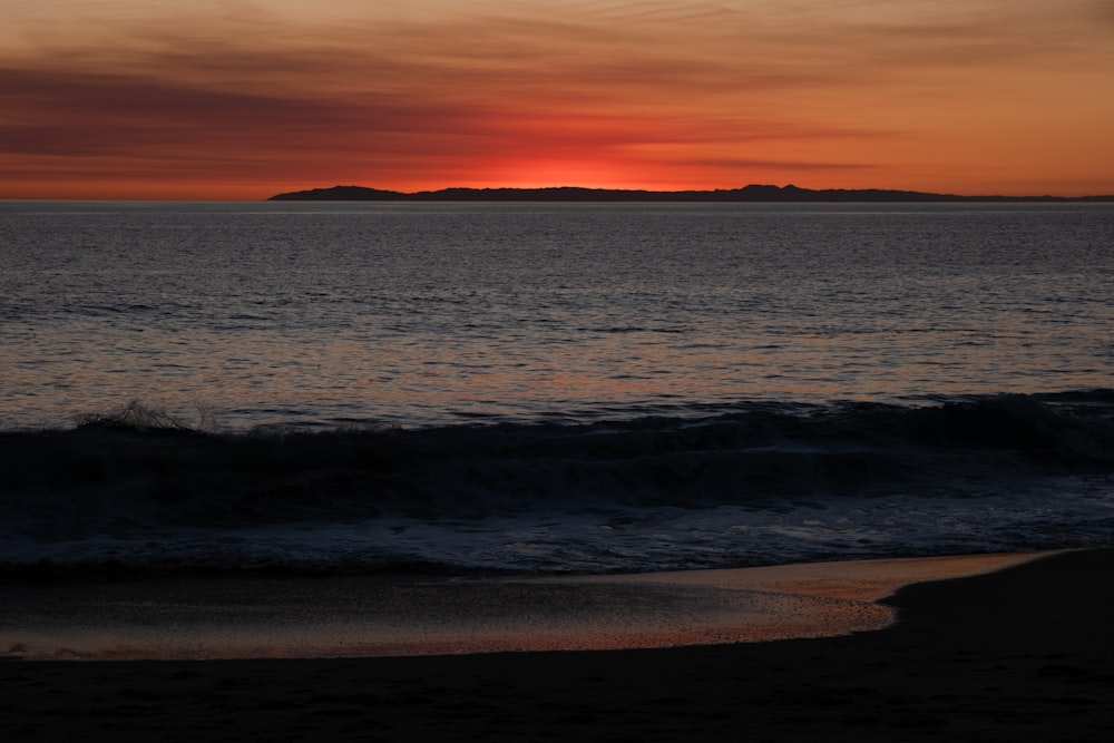 a sunset over a body of water with a small island in the distance