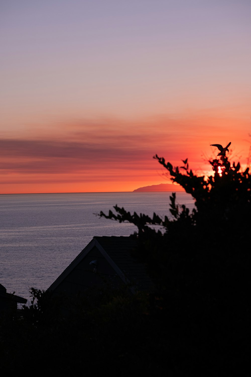 the sun is setting over the ocean with a house in the foreground