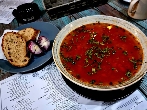 A colorful bowl of fresh vegetable soup with herbs on a rustic wooden table.