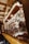 A market stall filled with various colorful sweets and treats. Gingerbread hearts with messages hang above a display of candies, candied apples, and chocolate-covered snacks. Soft yellow string lights and garlands with pine needles create a warm and festive atmosphere.