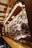 A market stall filled with various colorful sweets and treats. Gingerbread hearts with messages hang above a display of candies, candied apples, and chocolate-covered snacks. Soft yellow string lights and garlands with pine needles create a warm and festive atmosphere.