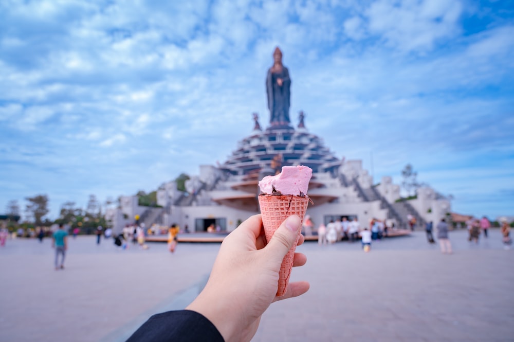 a hand holding an ice cream cone in front of a statue