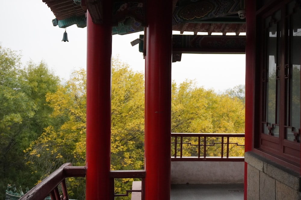 a balcony with red pillars and a view of trees