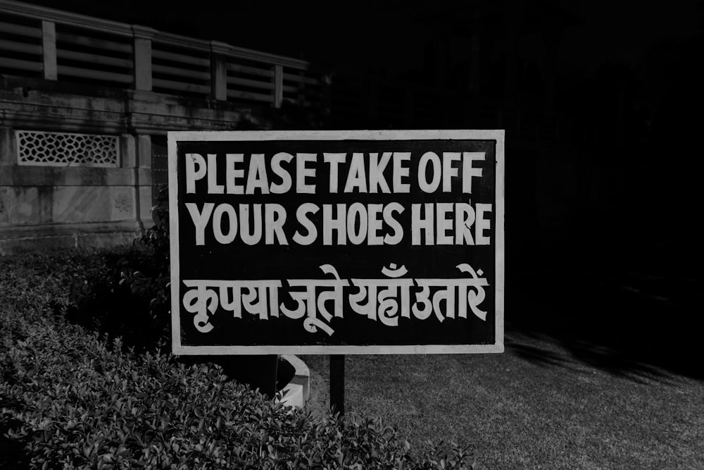 uma foto em preto e branco de uma placa que diz por favor tire seus sapatos aqui
