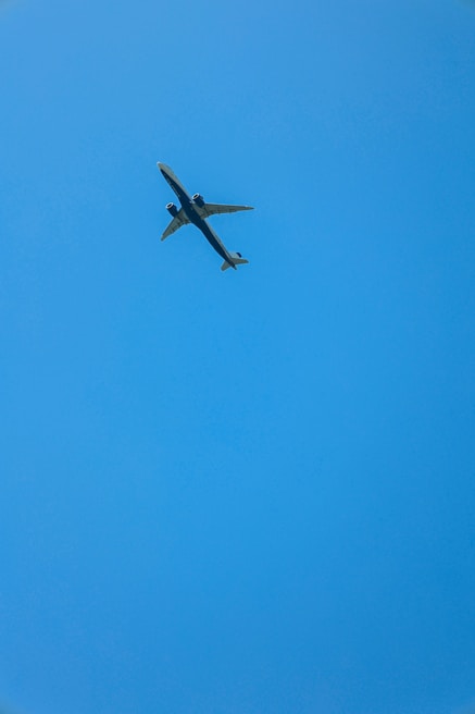 A commercial airplane flying through a clear blue sky, viewed from below. The aircraft appears to be mid-flight with its wings extended and engines visible.