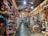 A vibrant, bustling indoor market stall filled with an array of colorful merchandise. The shelves are stocked with leather bags, hats, crafts, and various decorative items. The scene is lively, with bright colors and diverse items creating a visually rich environment.