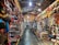 A vibrant, bustling indoor market stall filled with an array of colorful merchandise. The shelves are stocked with leather bags, hats, crafts, and various decorative items. The scene is lively, with bright colors and diverse items creating a visually rich environment.