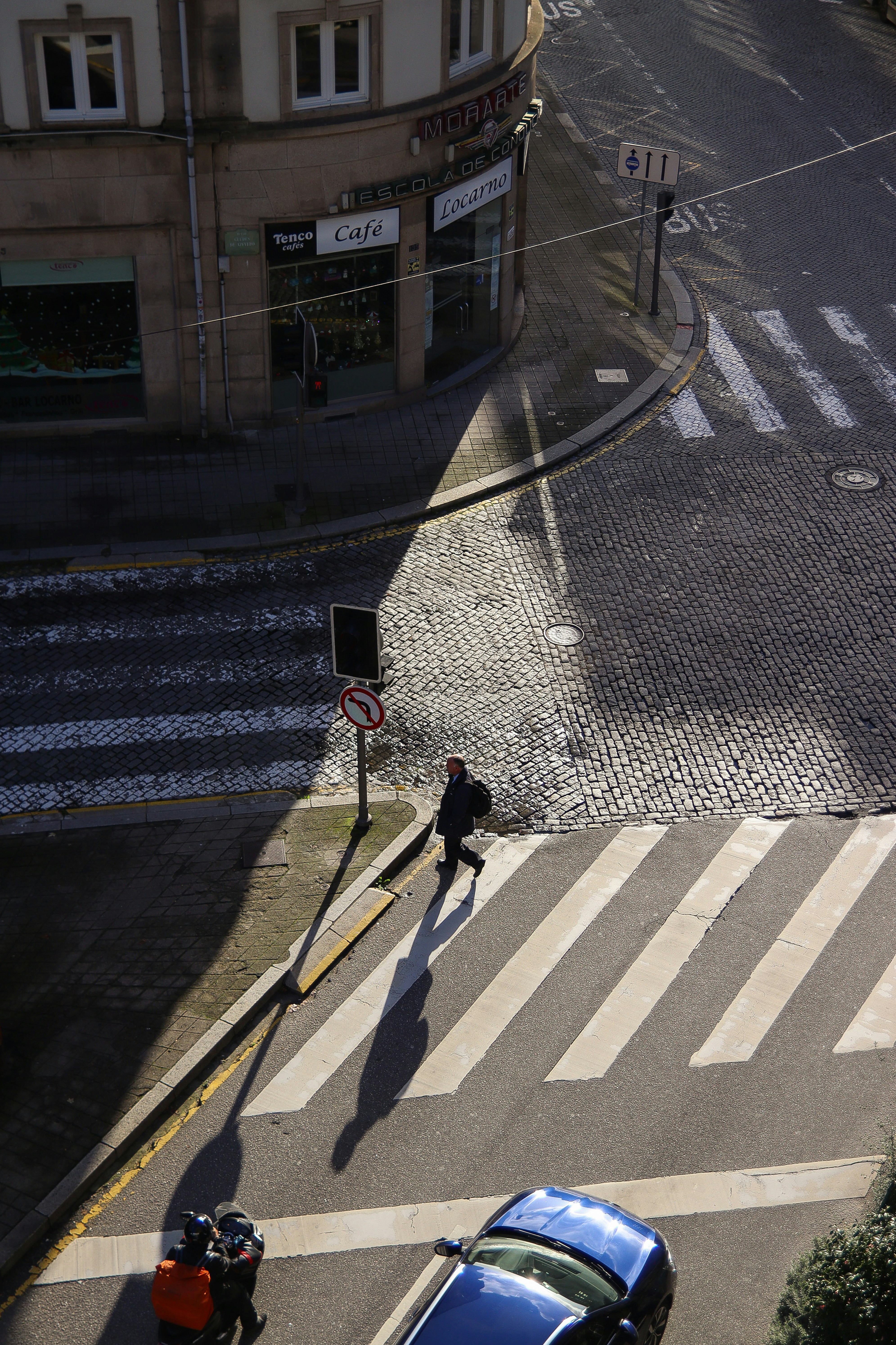 a person walking across a street next to a blue car
