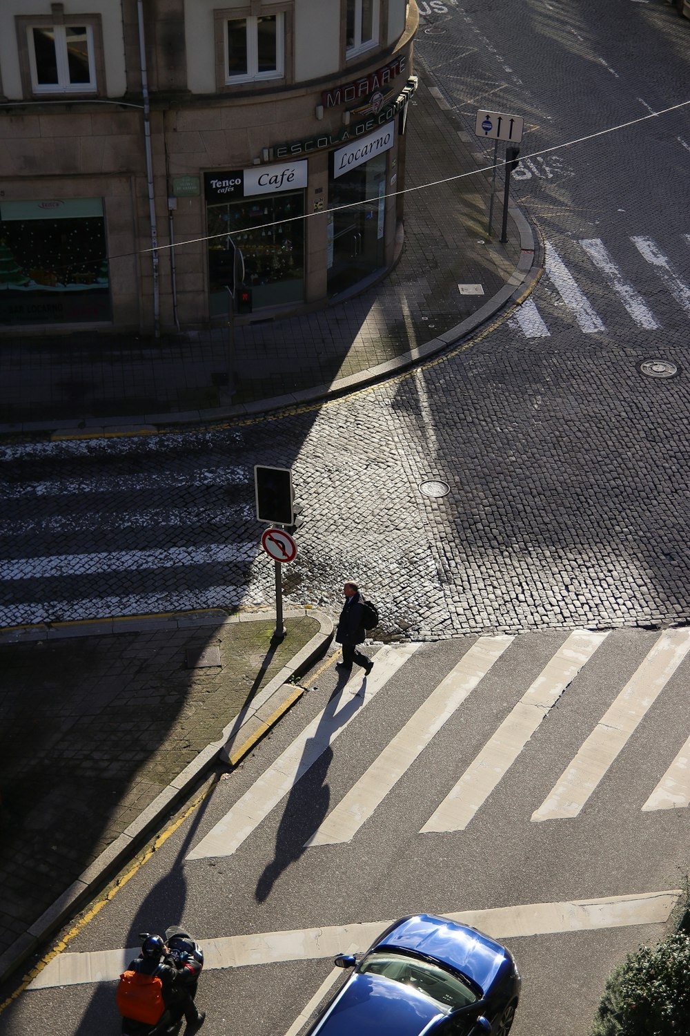 a person walking across a street next to a blue car