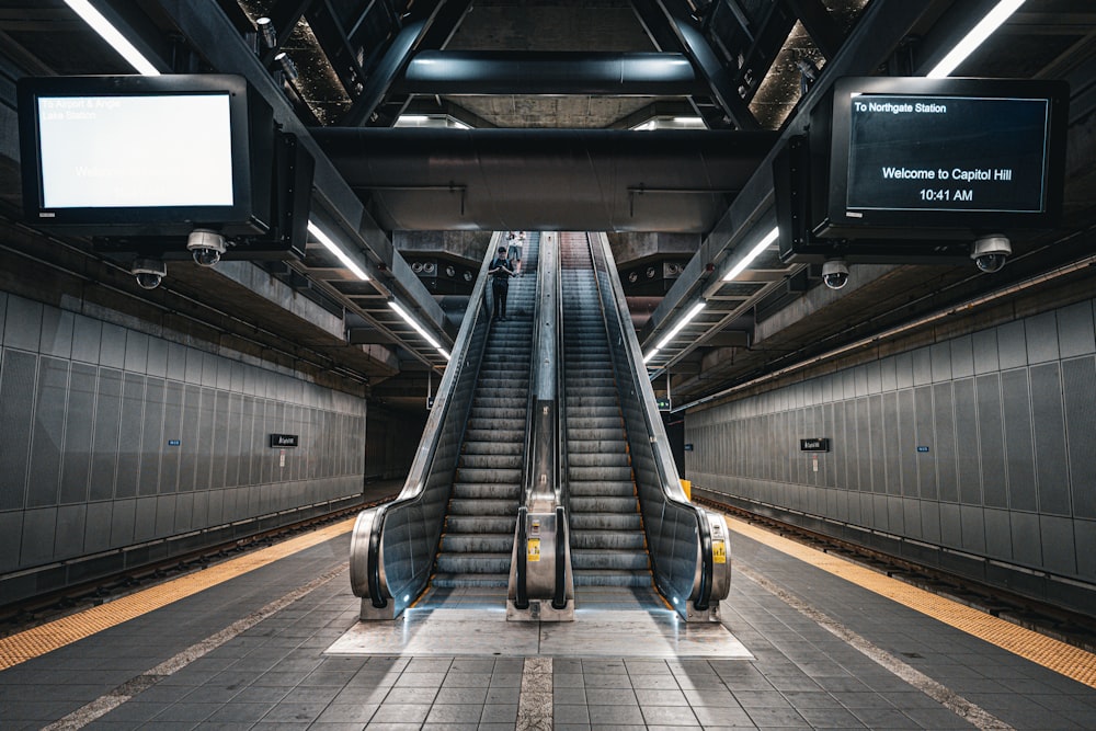 an escalator in a subway station with two monitors