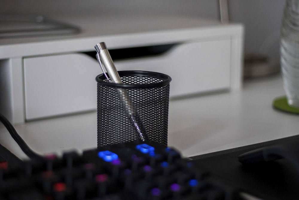 a pen is sitting in a cup next to a keyboard