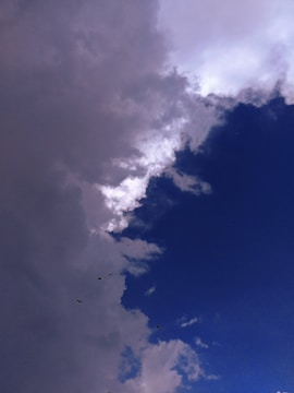 A dramatic contrast between dark, stormy clouds and a clear blue sky, with a few birds visible in flight.